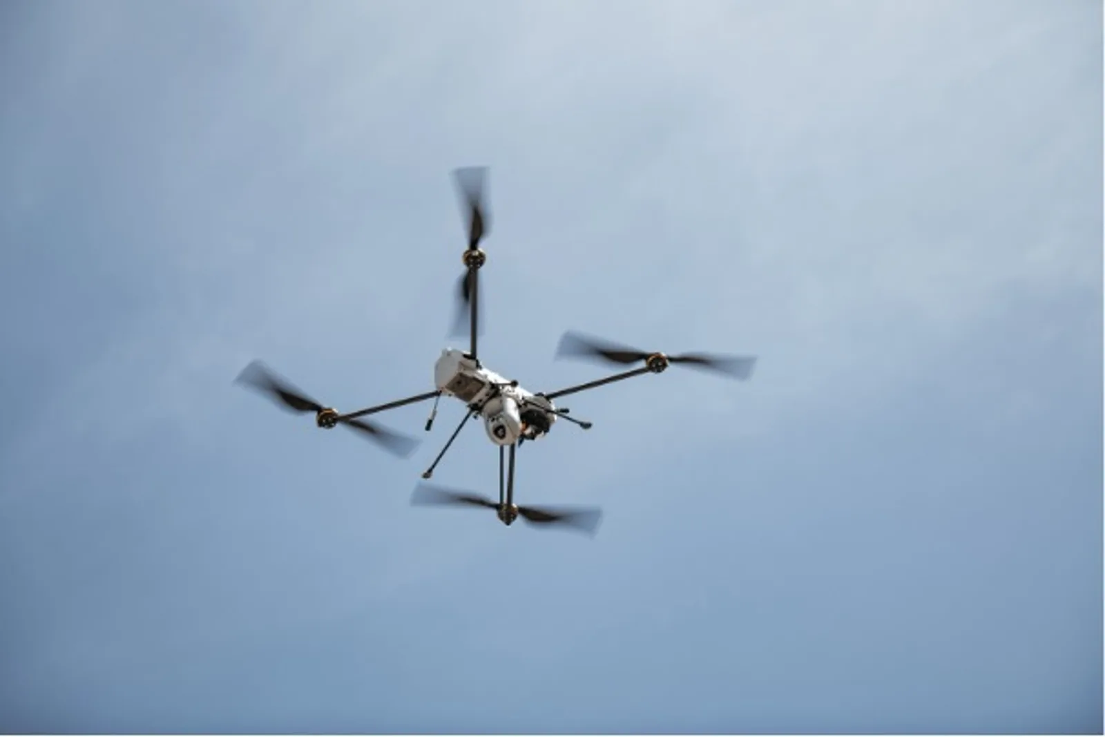 Quadrokopter von Leonardo mit montierter optronischer Sensoreinheit zur Zielbeleuchtung im Flug vor blauem Himmel
