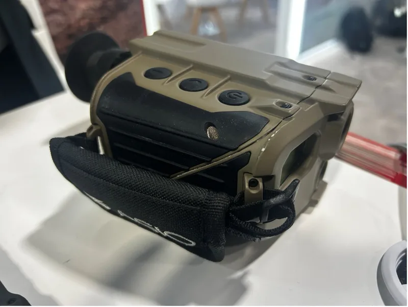 Elektro-optisches Handbeobachtungsgerät von Asio Technologies in sandfarbenem Gehäuse mit Bedientasten und Handschlaufe auf einem Messestand