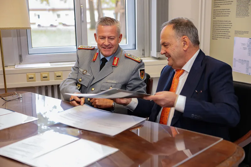 Generalleutnant André Bodemann unterzeichnet in Uniform an einem Besprechungstisch gemeinsam mit einem zivilen Partner Verträge
