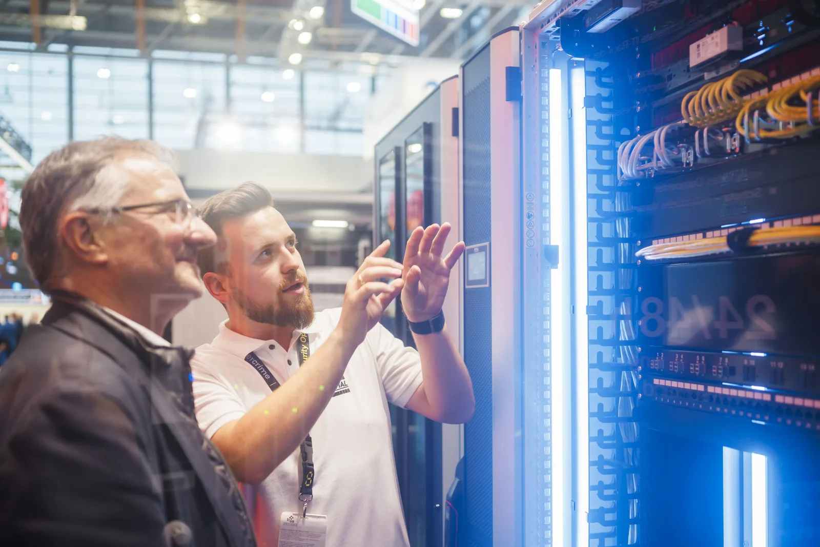 it-sa CONFERENCE: Zwei Männer betrachten und besprechen einen beleuchteten Serverschrank auf einer Messe