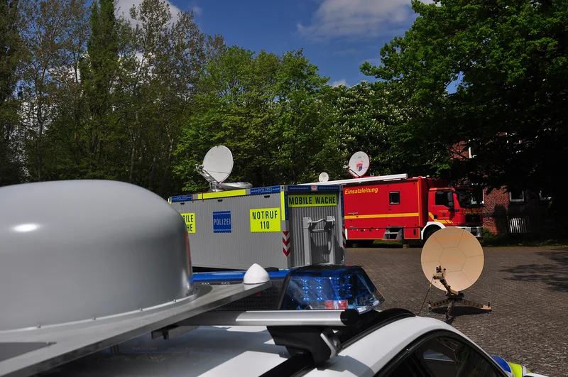 Polizei-Streifenwagen, mobiler Wachcontainer und rot-gelber Einsatzleitwagen mit ND SatCom-Satellitenantennen im Bereitstellungsraum