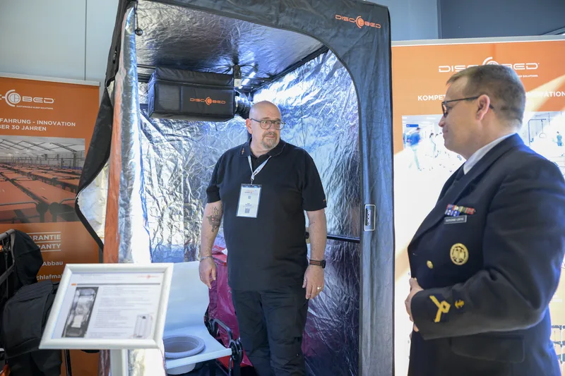Vertreter von Disc-O-Bed erläutert einem Offizier der Deutschen Marine eine mobile Zeltkabine mit Belüftungstechnik auf einer Fachmesse