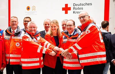 Vertreter aus Politik und DRK legen vor einer Wand mit DRK- und Zivilschutzreserve-Schriftzügen symbolisch die Hände zusammen
