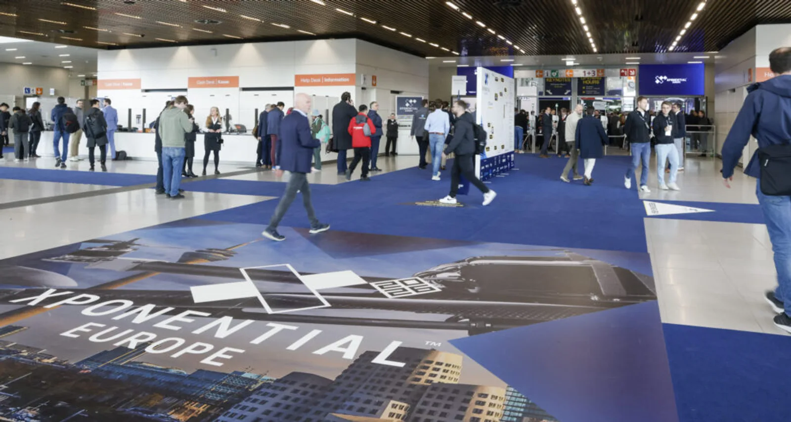 Besucher im Eingangsbereich der Fachmesse XPONENTIAL Europe vor einer Bodenwerbung für unbemannte Systeme mit Registrierungsschaltern
