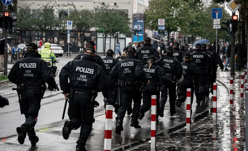 Protest: Gruppe uniformierter Polizisten im Laufschritt auf regennasser Straße, daneben ein Motorradpolizist