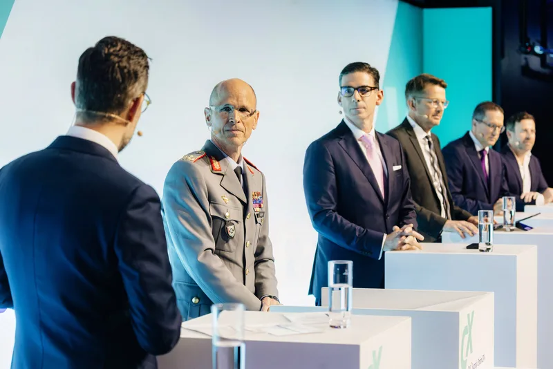 Bundeswehr-General im Dienstanzug und zivile Teilnehmer bei einer Podiumsdiskussion der Bundesvereinigung Logistik mit Moderator