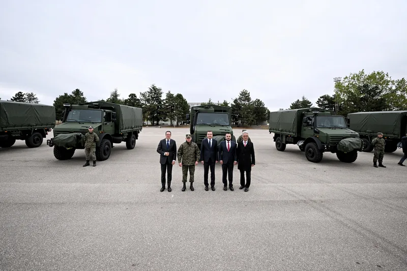 Politik- und Militärdelegation vor Mercedes-Benz Unimog-Lastkraftwagen mit Soldaten in Flecktarnuniform auf einem Freigelände